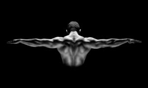Rear view of healthy muscular man with his arms stretched out isolated on black background